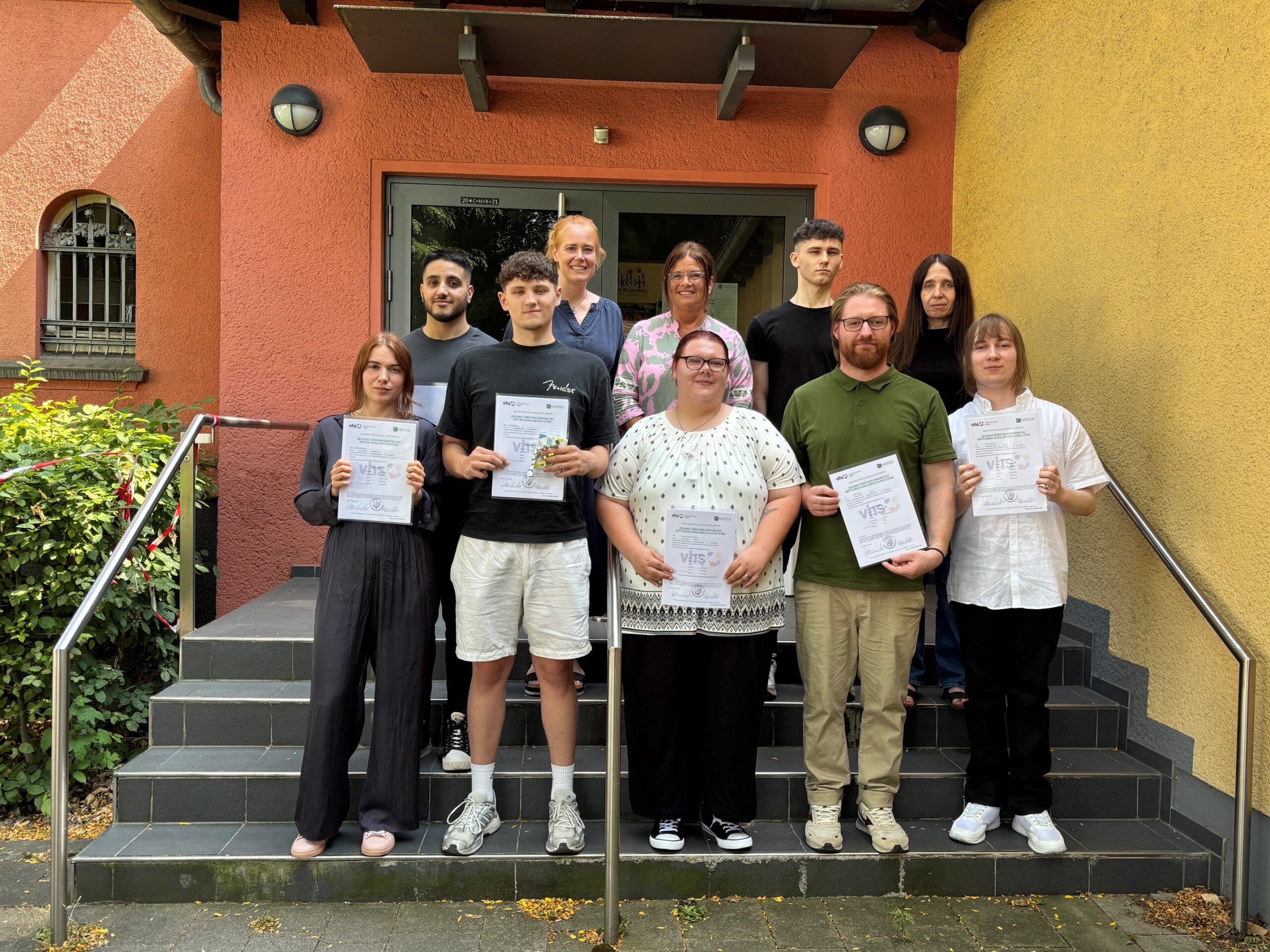 Gemeinsam mit der stellvertretenden Bürgermeisterin Silvia Godde (Mitte hinten) sowie Christine Fester (2. v. l. hinten) und Vanessa Drosten (rechts hinten) von der VHS freuen sich (v. l. n. r.) Helena Sichtermann, Mahdi El Sayed, Neo Davis Wolny, Michaela Stratmann, Robbie Thomas Korth, Tobias Bialluch und Slawomir Juszczyk.